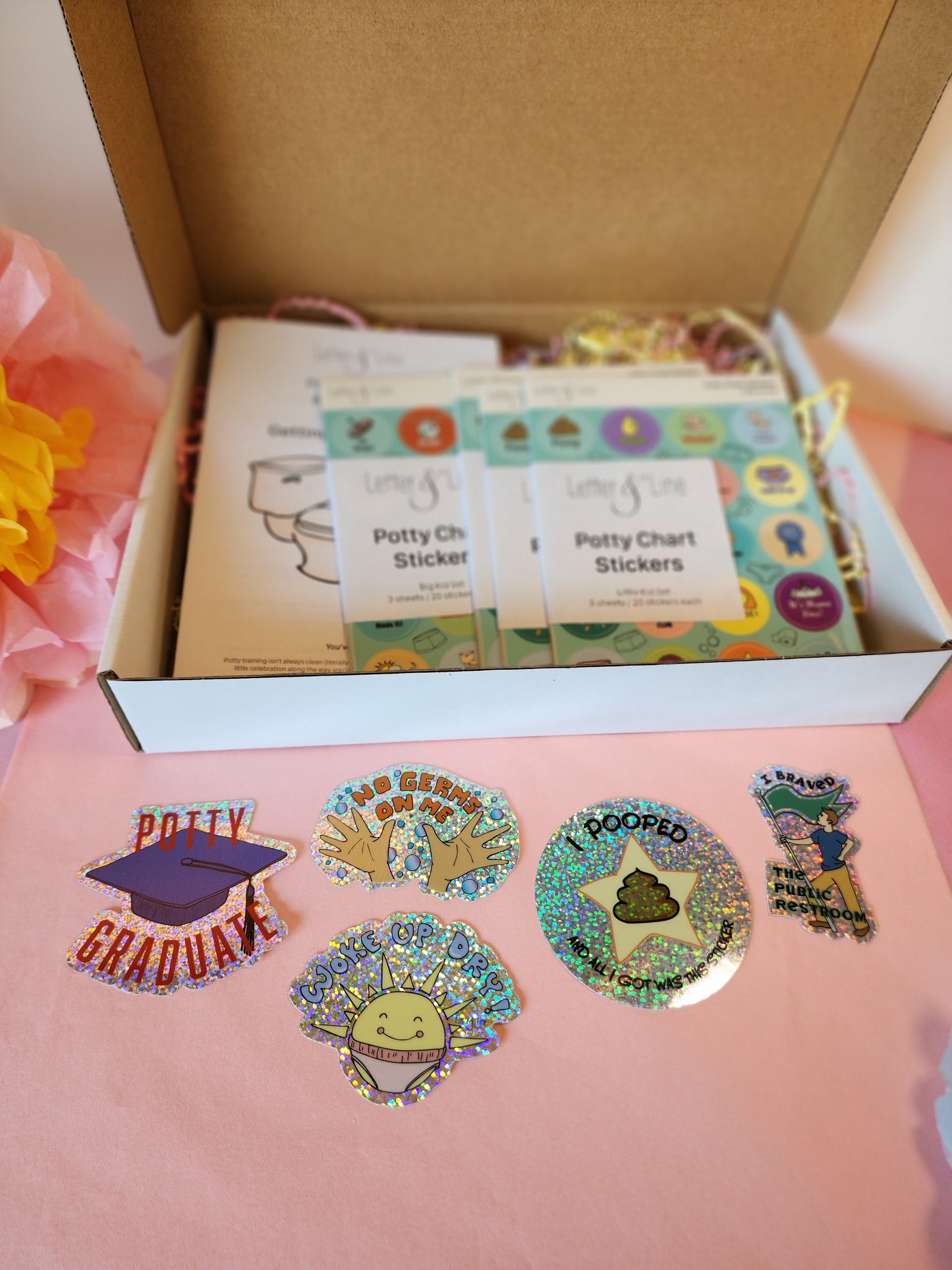 Flat lay of the five glitter potty stickers included in the potty training kit, arranged on the table in front of the open box