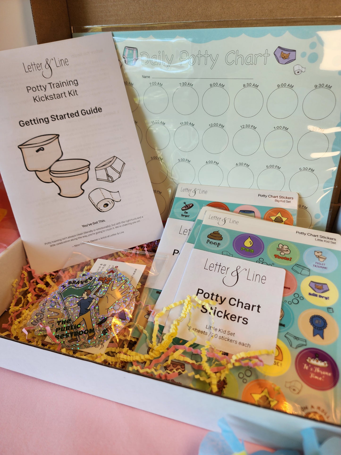 Open potty kit box on a pink background with all contents visible: chart, guide, two sticker sets, glitter stickers, and shredded filler.