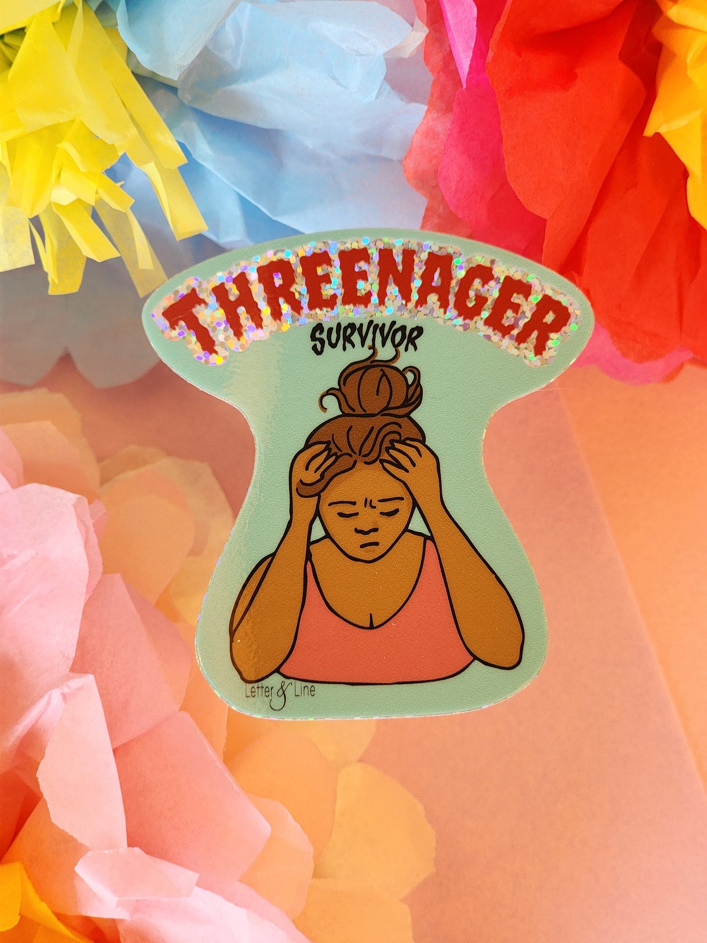Single “Threenager Survivor” sticker with a mom holding her head in hands illustration placed on a light pink background with layered pastel and bright tissue paper flowers.