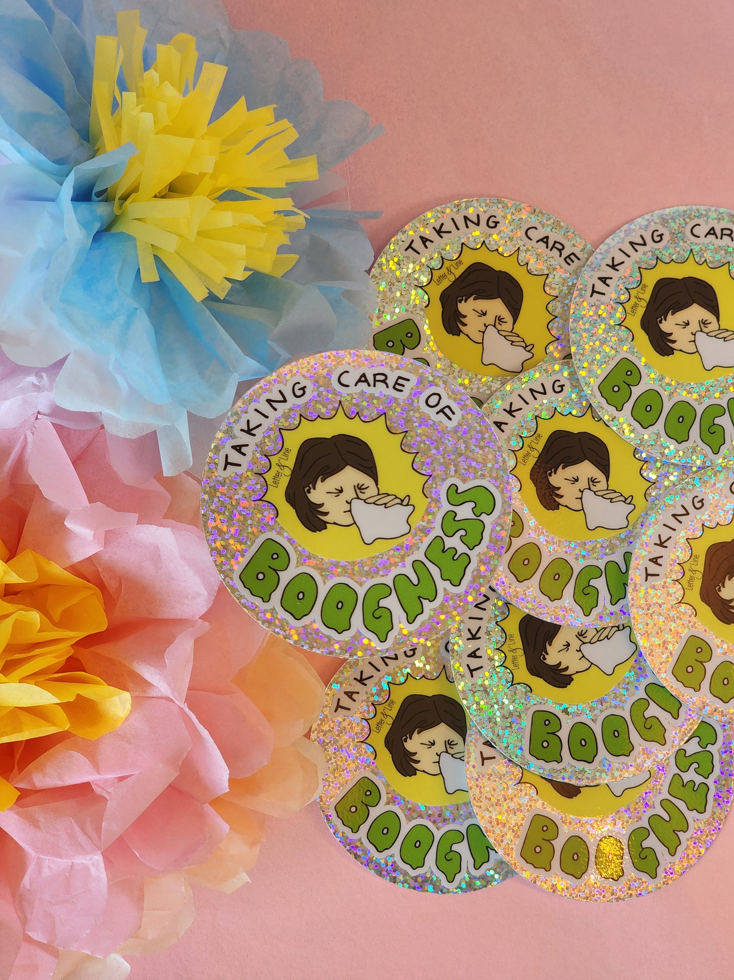 Several “Taking Care of Boogness” stickers scattered on a pink background surrounded by pastel tissue flowers.