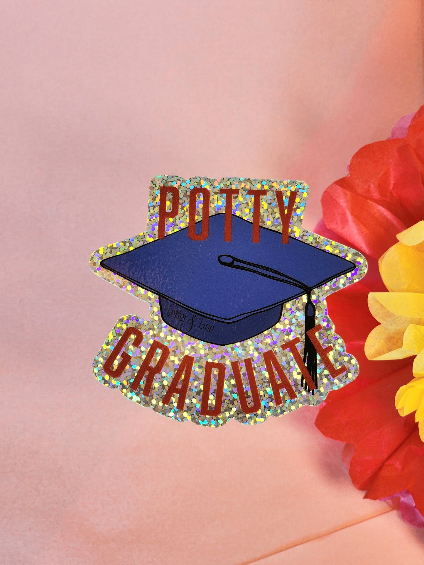 “Potty Graduate” sticker featuring a graduation cap and red lettering, framed by bright red and yellow tissue paper flowers.