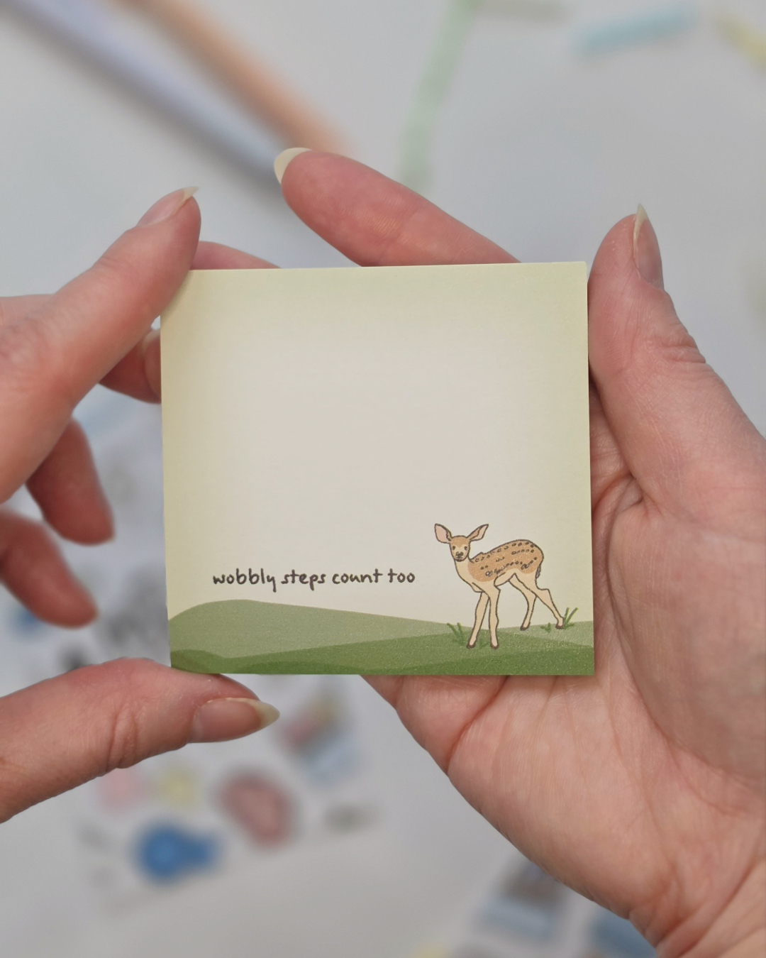 Hand holding Wobbly Steps Count Too deer illustrated Post-it Note pad showing size and scale
