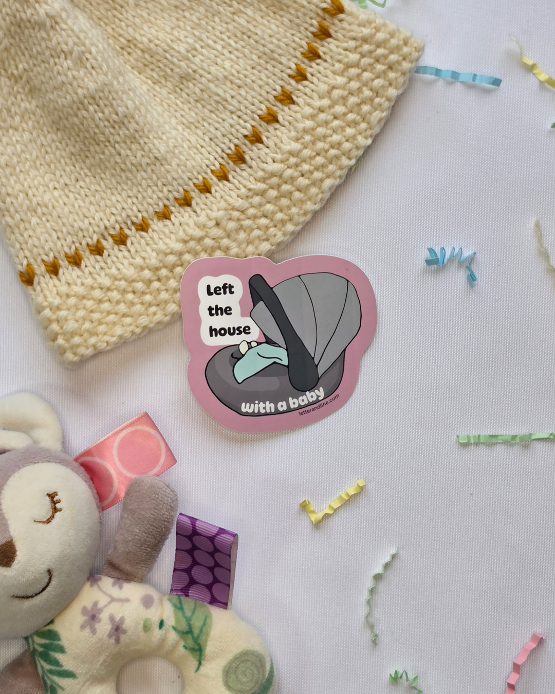 Left the House with a Baby new parent milestone sticker styled with a knit baby hat and stuffed animal on a white background