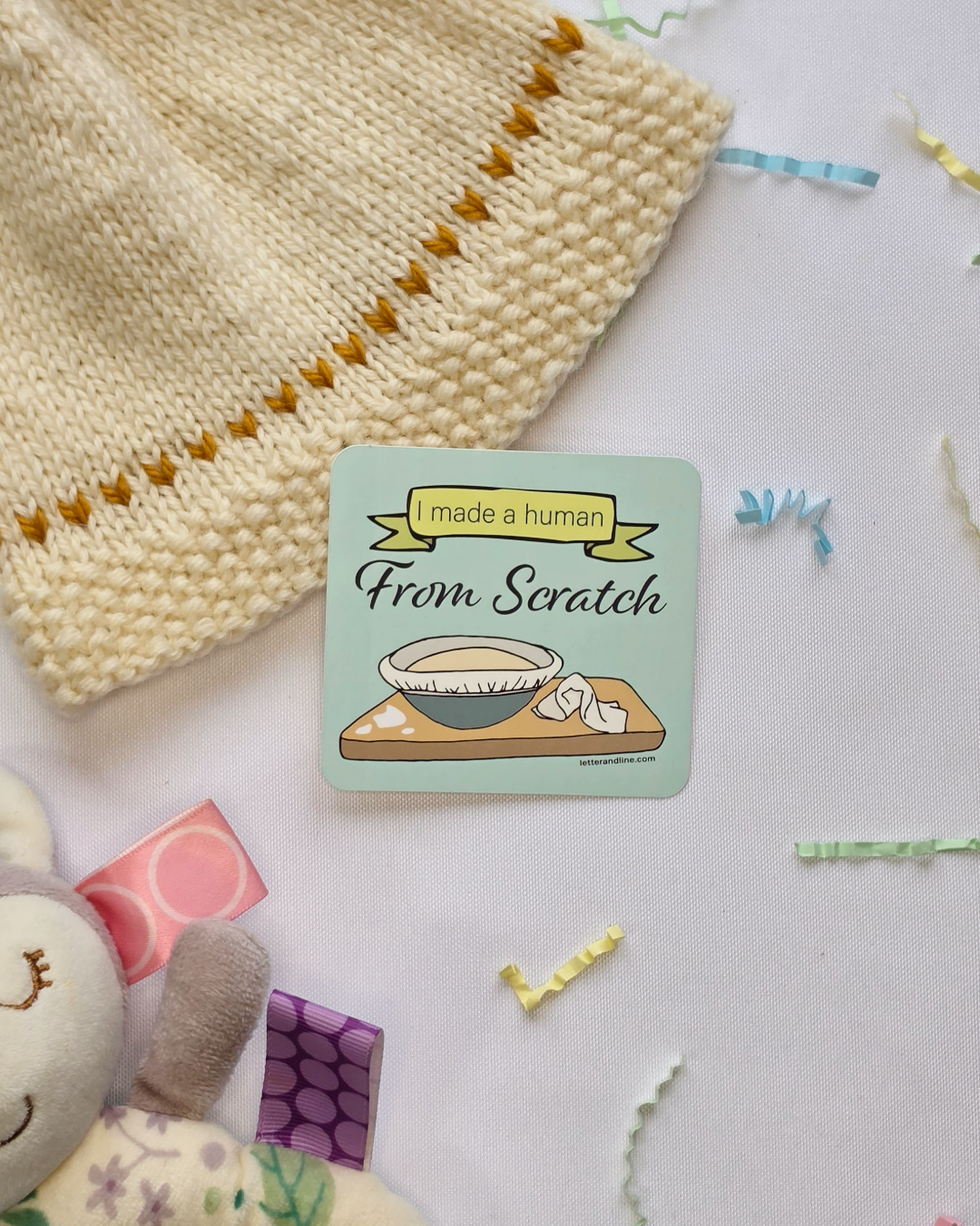 I Made a Human From Scratch milestone sticker styled with a knit baby hat and colorful paper confetti