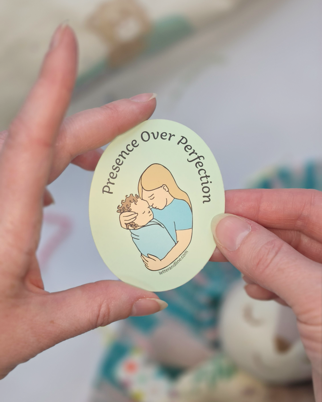 Hand holding Presence Over Perfection new parent milestone sticker showing illustrated parent cradling newborn design