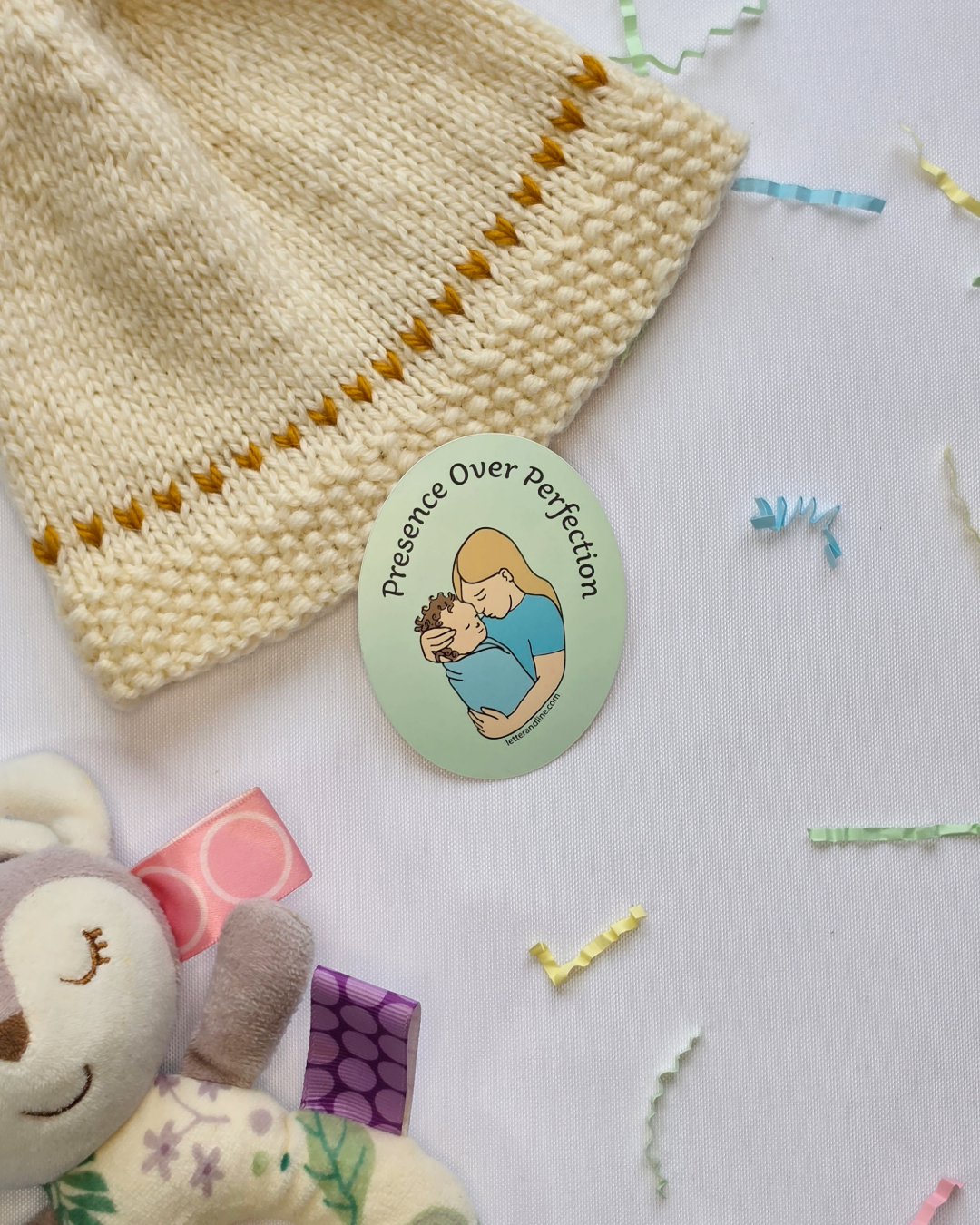 Presence Over Perfection milestone sticker styled with a knit baby hat and colorful confetti and baby items