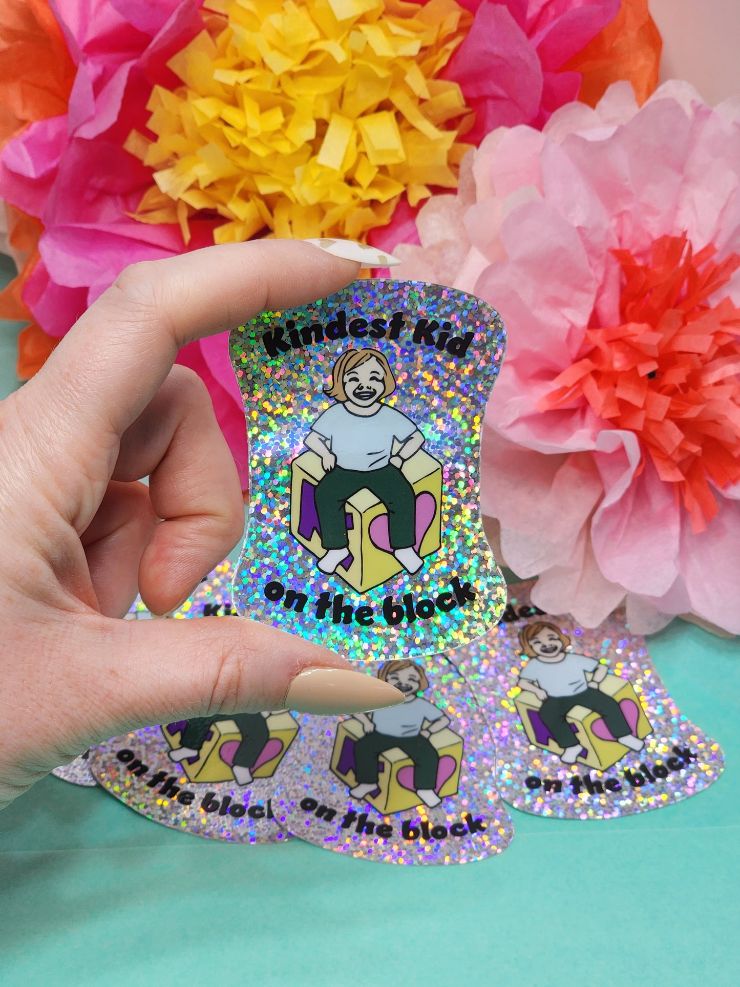 close-up of “Kindest Kid on the Block” glitter sticker tilted to show holographic sparkle