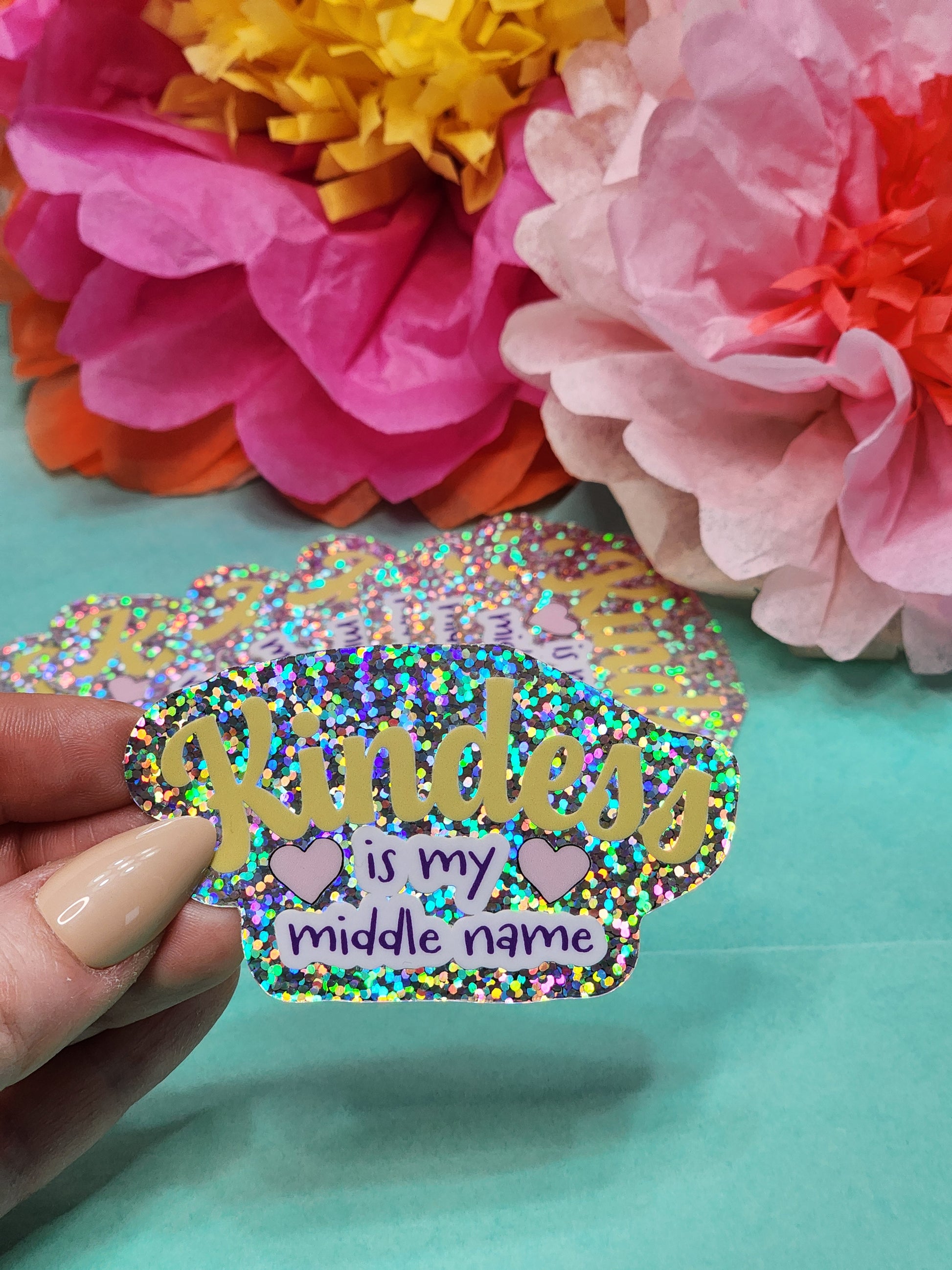close-up of “Kindness is my middle name” glitter sticker with a small stack of matching stickers behind it