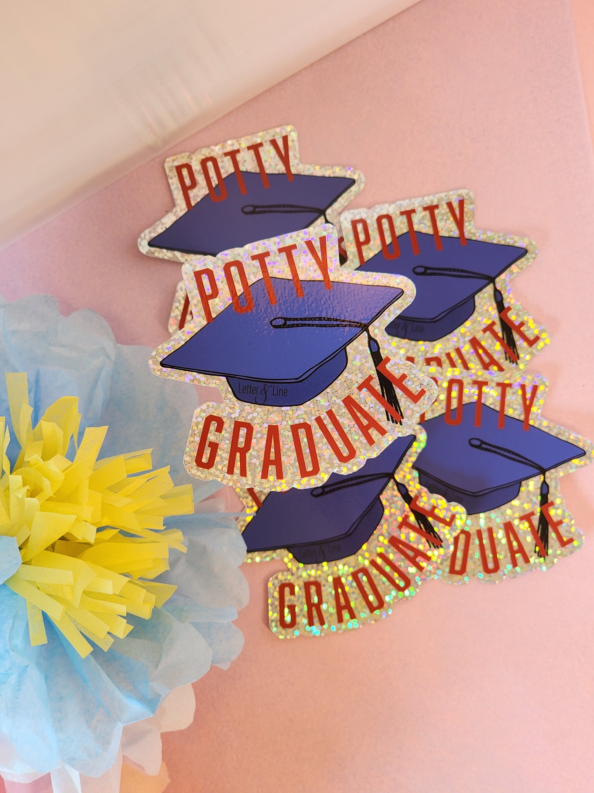 Multiple “Potty Graduate” stickers arranged in a cluster on a pink surface with pastel flowers surrounding them.