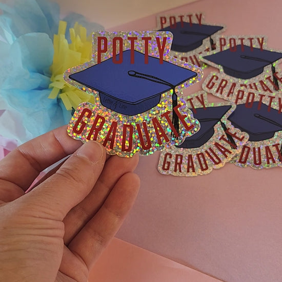 Video preview of a hand turning the “Potty Graduate” sticker to show its glitter effect, set against a soft floral background.